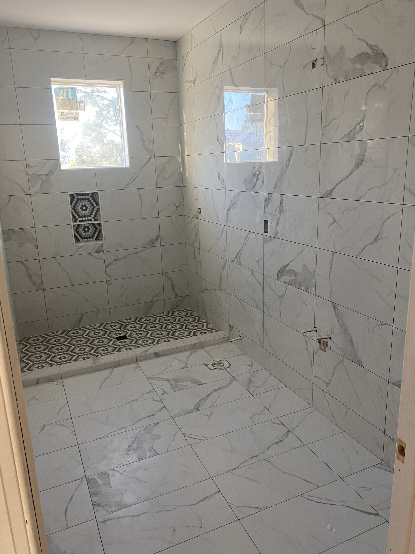 Marble-look tiled shower with patterned mosaic floor and niche
